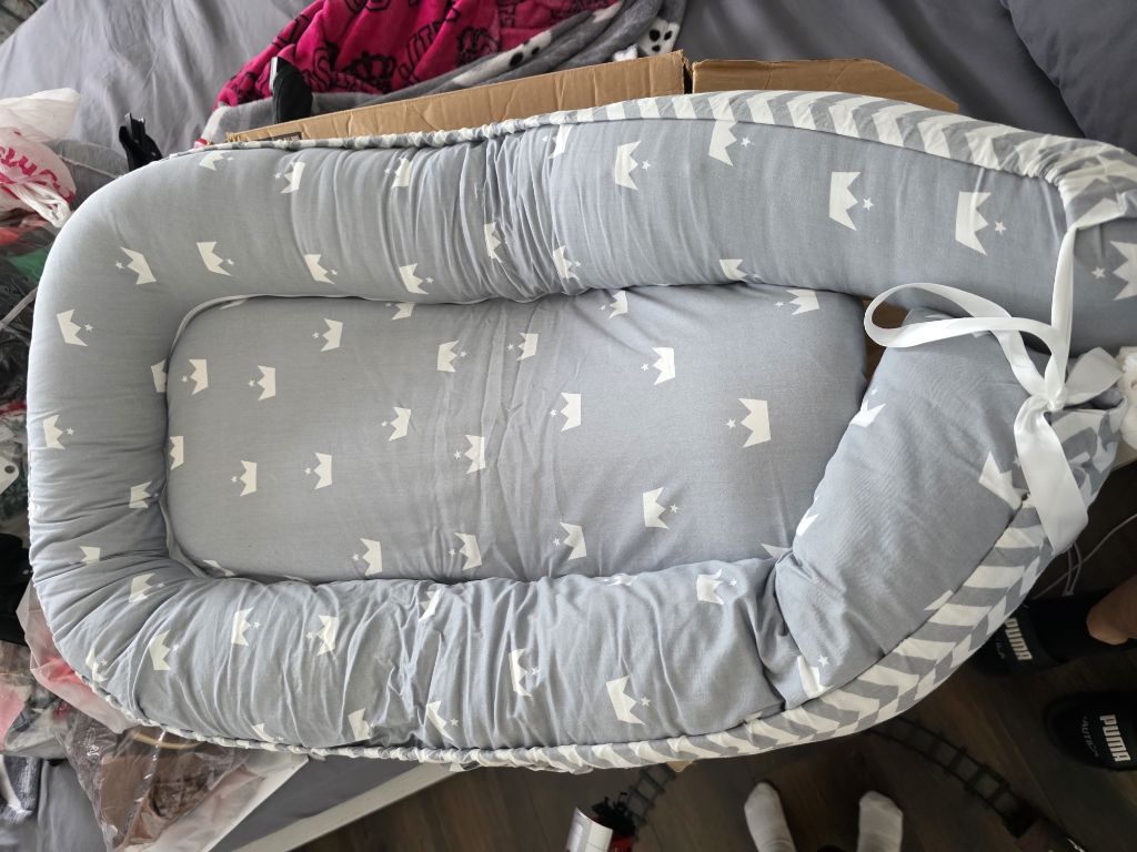 Free Este es un nido reductor para bebé portátil de color gris con estampado de coronas